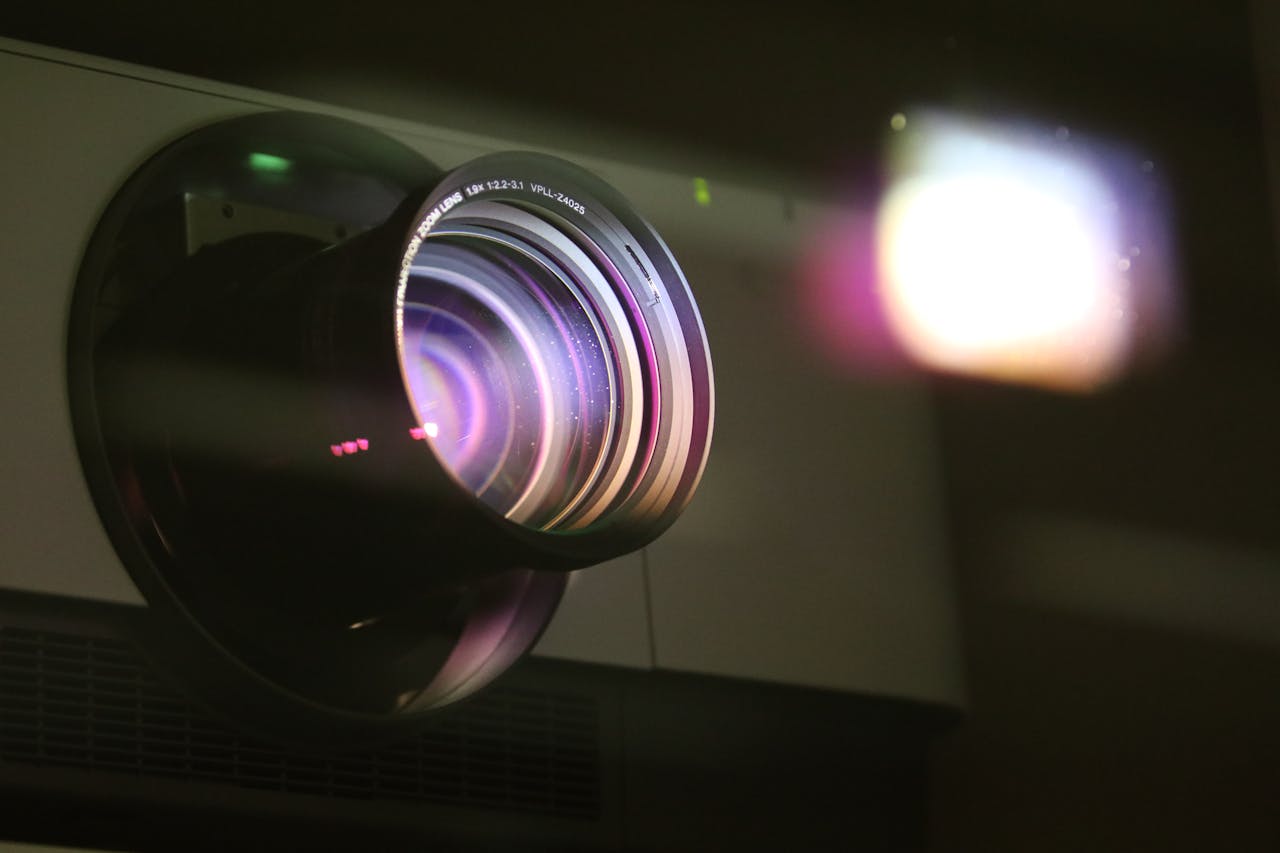 Home Detailed view of a projector lens emitting light, showcasing optical technology.
